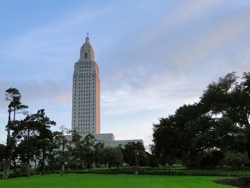 A tall, art deco-style building stands among trees and green lawns under a partly cloudy sky.