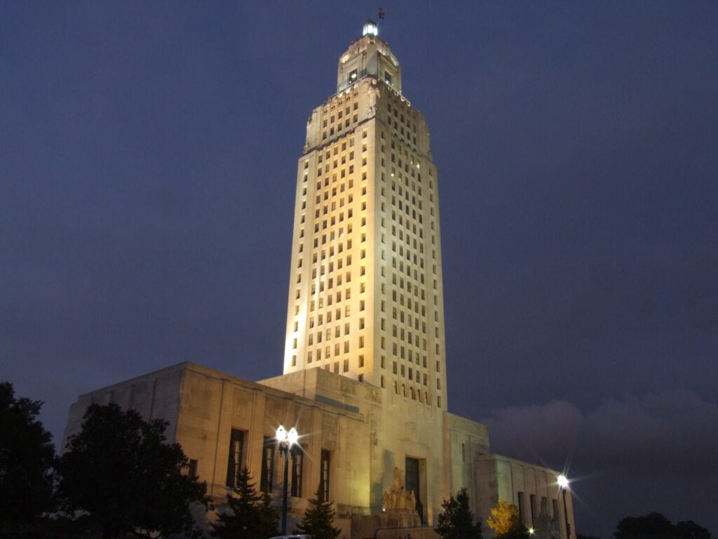 Tall art deco government building illuminated at night, with a central tower rising above a lower rectangular base against a dark sky.