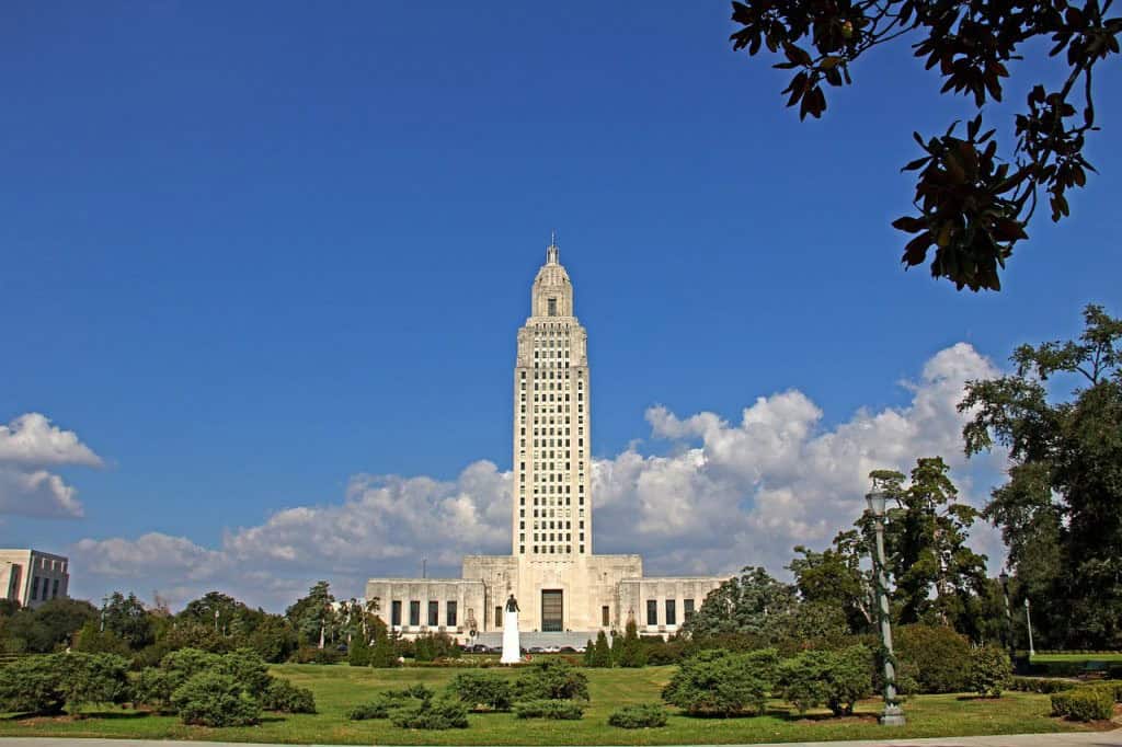 A tall, white art deco building stands at the midpoint of a green lawn under a blue sky with scattered clouds.