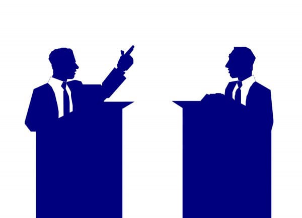 Two men in suits stand at podiums, engaging in a fiscal debate or discussion.