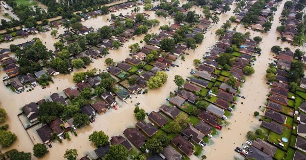Aerial view of a Houston neighborhood with streets and houses flooded by muddy water—our thoughts and prayers are with those affected.