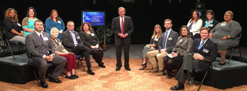 A group in business attire sits in a studio around a man standing by a Louisiana Public Square sign, discussing why education matters.