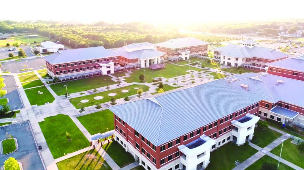 Aerial view of a modern school campus with red-brick buildings and green lawns, celebrating its anniversary under bright sunlight.
