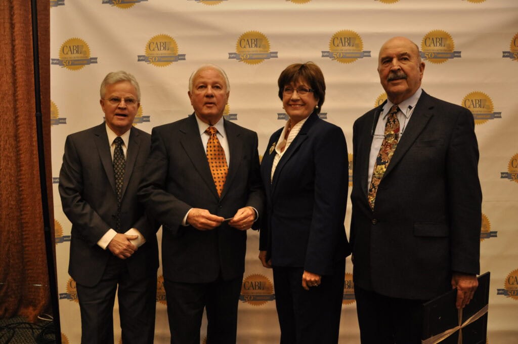 Four leaders in business attire stand before a step-and-repeat backdrop showcasing the CARH 50th anniversary logo.