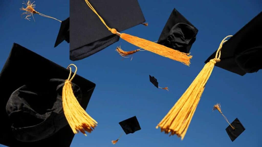 Several students toss black graduation caps with gold tassels into a clear blue sky, celebrating as they graduate.