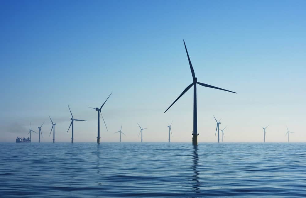 Multiple offshore wind turbines stand in the ocean, representing Gulf energy and a cleaner energy future under a clear blue sky.