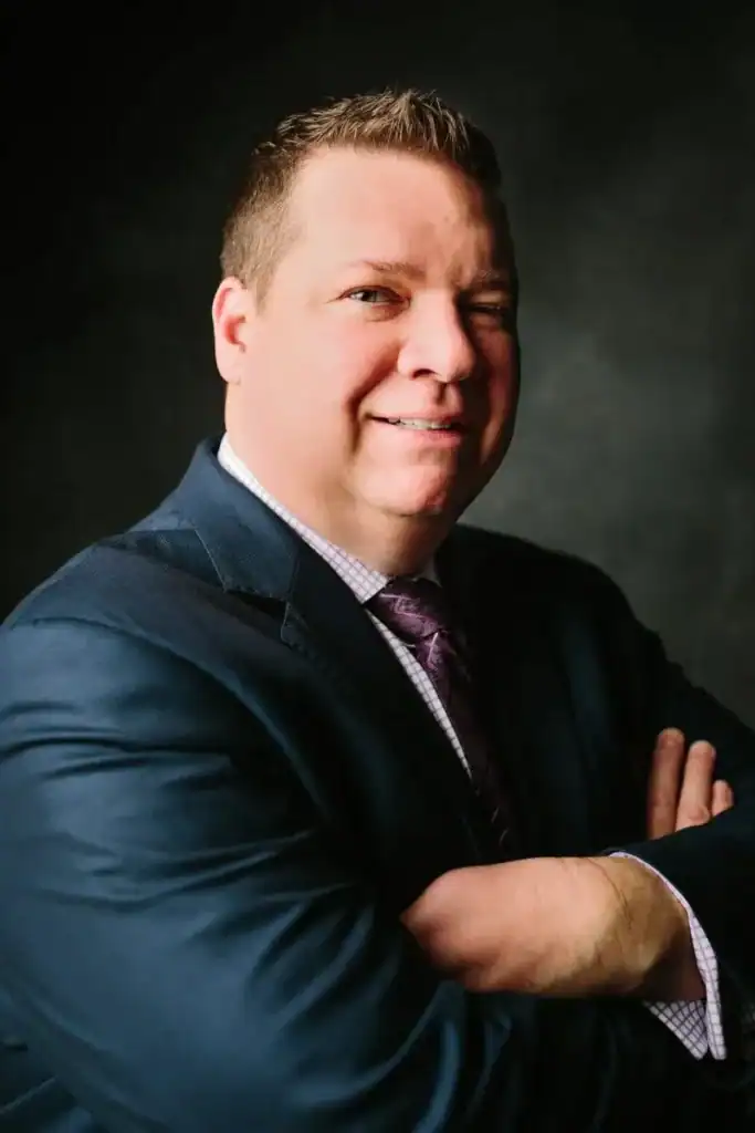 William Weaver, of the Committee of 100, stands with arms crossed and a slight smile against a dark background.