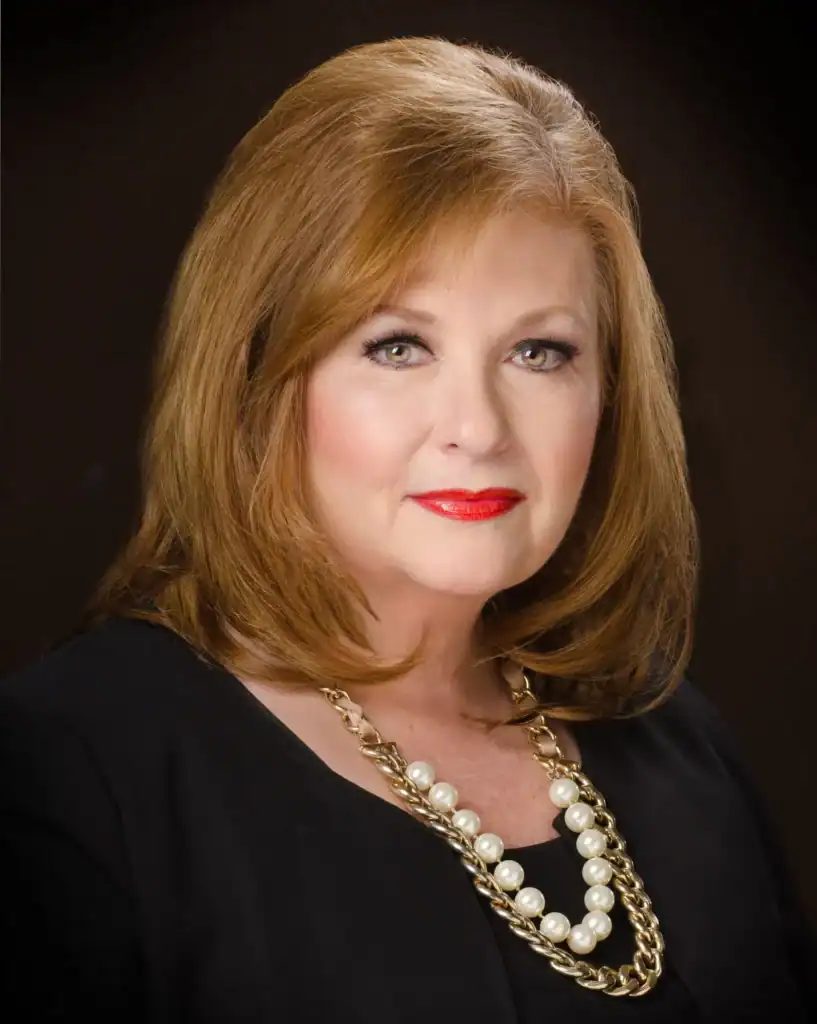 A woman with shoulder-length red hair, dressed elegantly, poses against a dark background at the CENLA Chamber Annual Legislative Briefing.