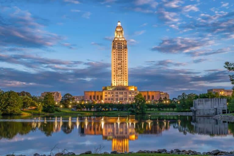 The Louisiana Capitol building in Baton Rouge illuminated at dusk, reflecting off of the Mississippi River.