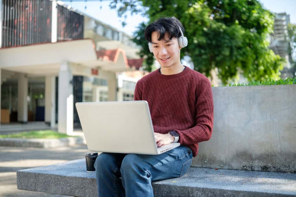 A person wearing headphones and a red sweater, perhaps a Leadership Louisiana participant, works on a laptop outside with coffee nearby.
