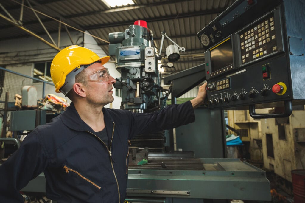 A factory worker in a yellow hard hat operates a CNC machine, showcasing Leadership Louisiana in an industrial setting.